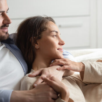 Warm embraces of love. Caring young spouses or couple in love spending free time at home together sitting on sofa embracing looking at distance enjoying each other company dreaming of happy future