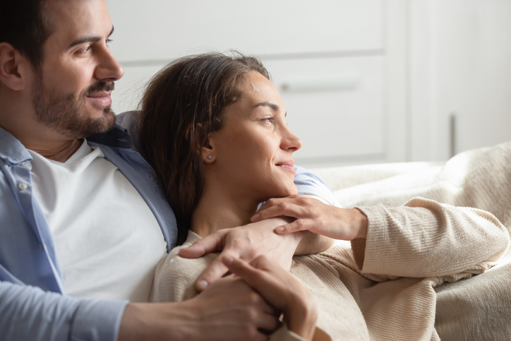 Warm embraces of love. Caring young spouses or couple in love spending free time at home together sitting on sofa embracing looking at distance enjoying each other company dreaming of happy future