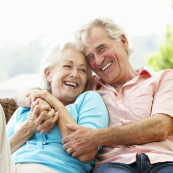 Senior Couple Sitting On Outdoor Seat Together Laughing