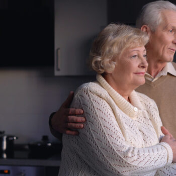 An old man putting his hand on his wife's shoulder, offering support and care in their marriage and family